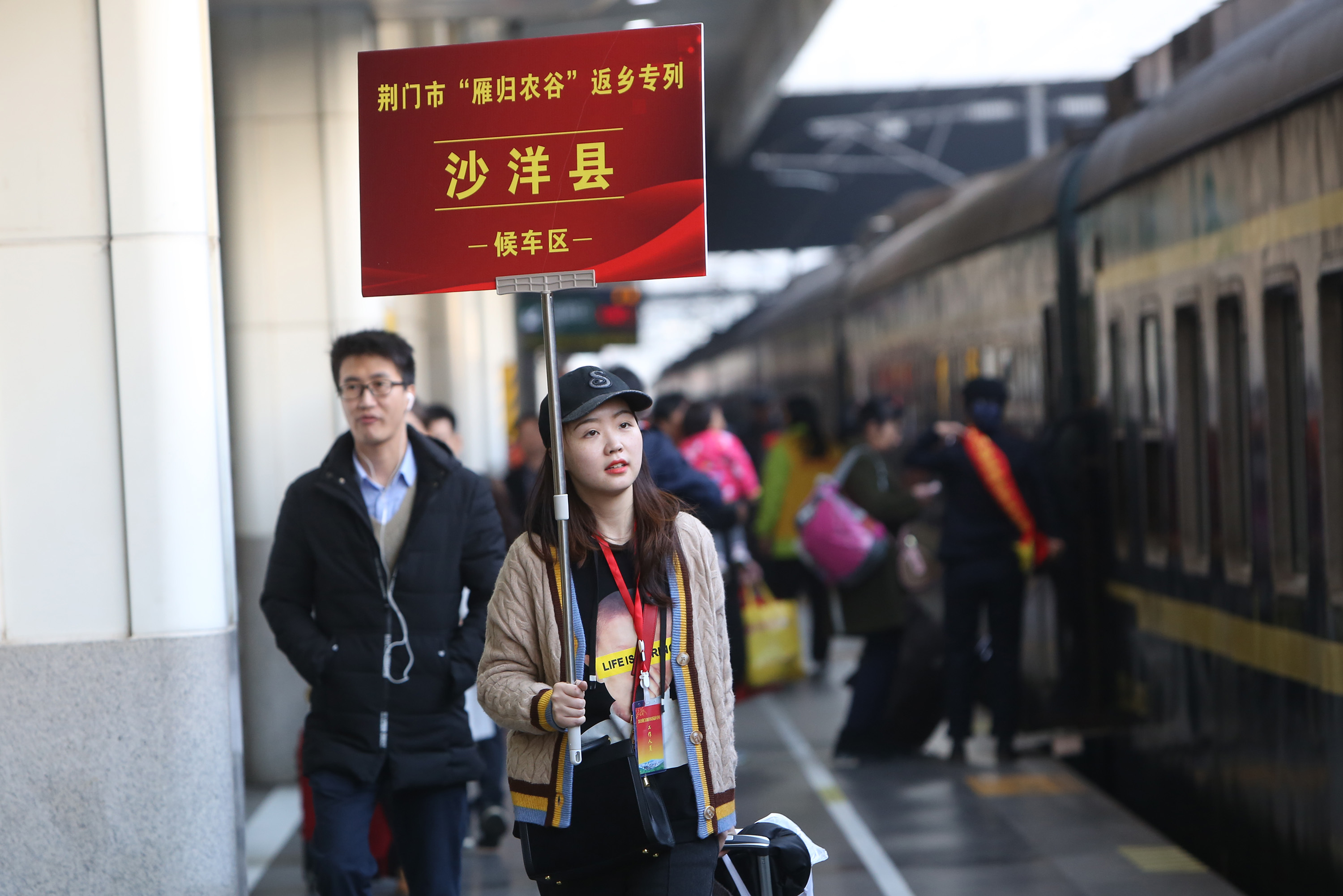 工作人员举着牌子引导旅客上车.