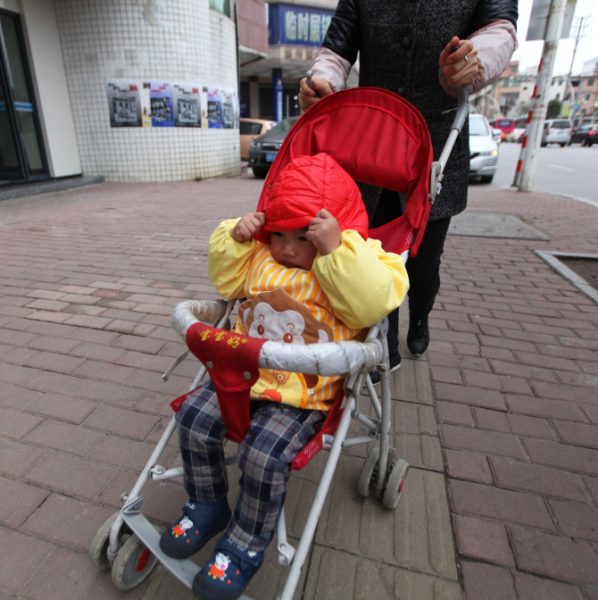 "暖"宝宝 寒风吹过,一名在街头坐着推车的宝宝用小手紧紧拉着帽檐遮挡