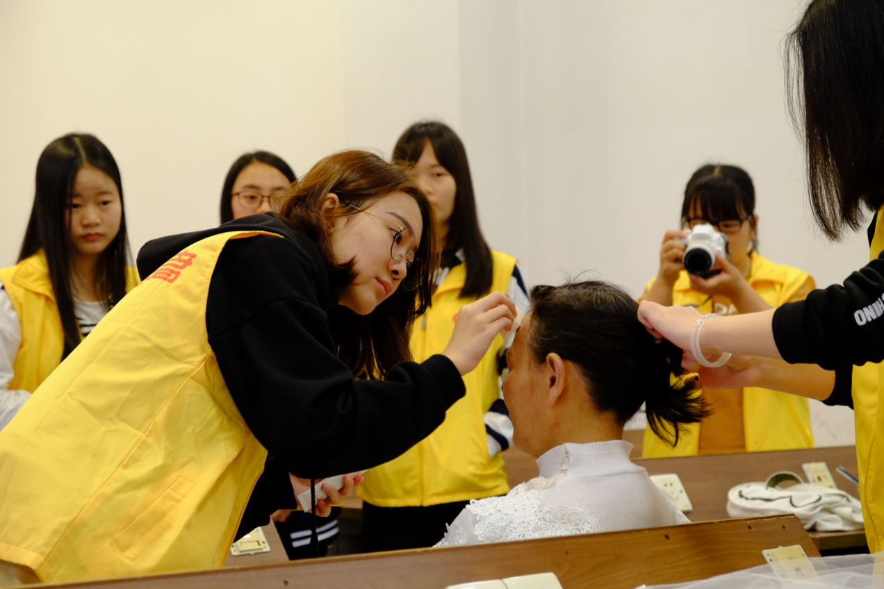 东软学院艺术团的同学们在给阿姨化妆。