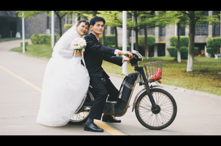 夏巨明和王麦珍在校园骑着电动车，被摄影师抓拍温馨画面。