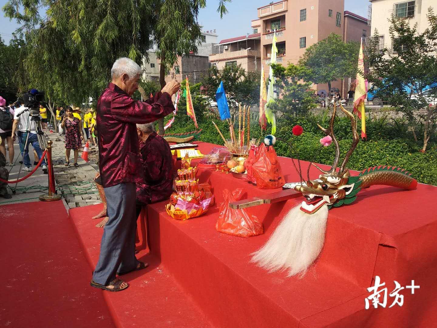 盐步老龙礼俗传承人邵钜熙在准备起龙仪式所需的祭品，而在祭台旁边，村民们也在敲锣打鼓助兴，好不热闹。邵钜熙介绍，盐步老龙已有586年历史。盐步老龙与泮塘龙舟在比赛中接下友谊的故事在珠三角甚至全国都是很少见的。我们要把祖祖辈辈传承了几百年的礼让和友爱精神继续传递下去。