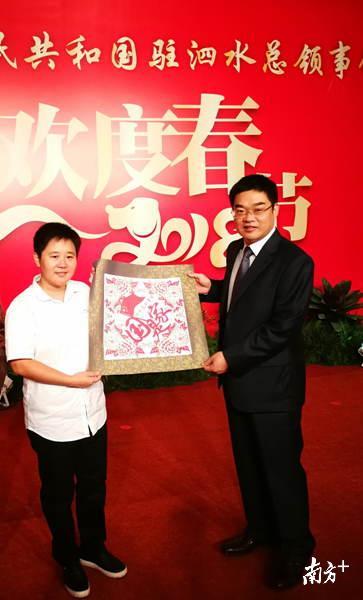 2018年2月5日，谢秀珠（左）受邀参加了印尼泗水总领馆的春节晚宴，将自己的原创客家剪纸《国是家》作为赠礼送给了总领事馆。（受访者供图）