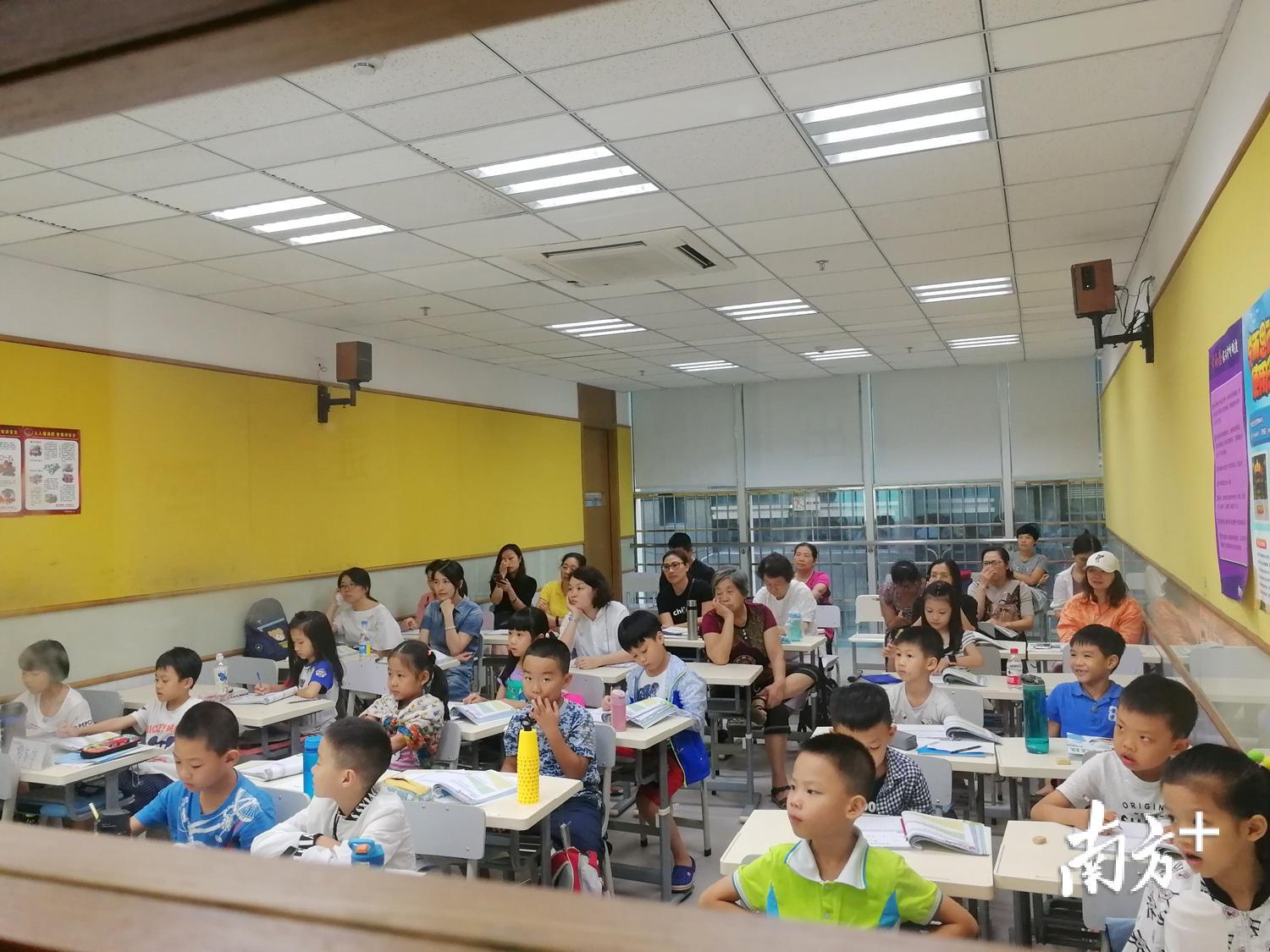一校外培训机构教学点的教室内，学生们正在上课，家长们在陪读。