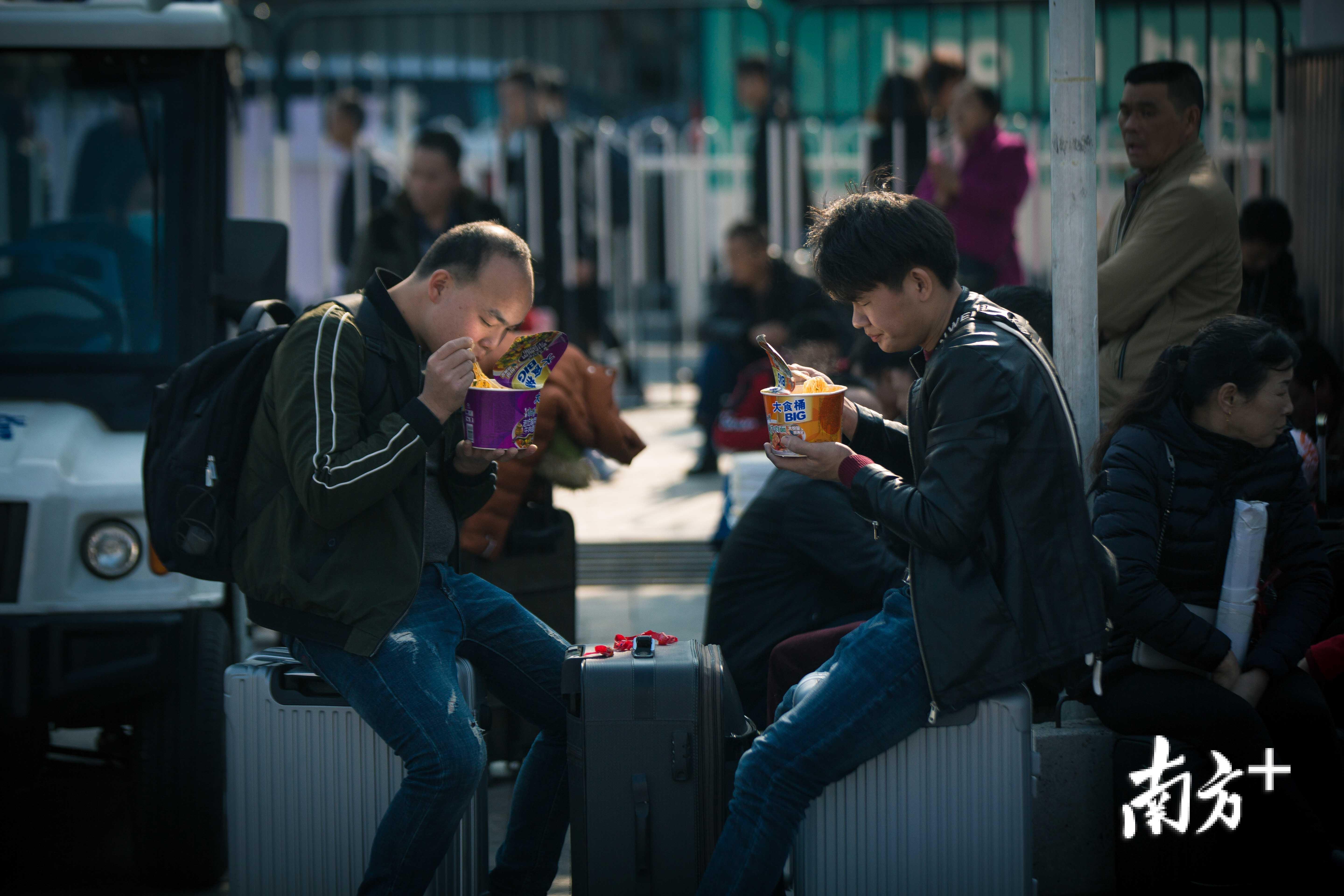 广州火车站前广场上，两个对向着吃方便面的男子恰好被面桶盖的锡箔纸打亮脸部。