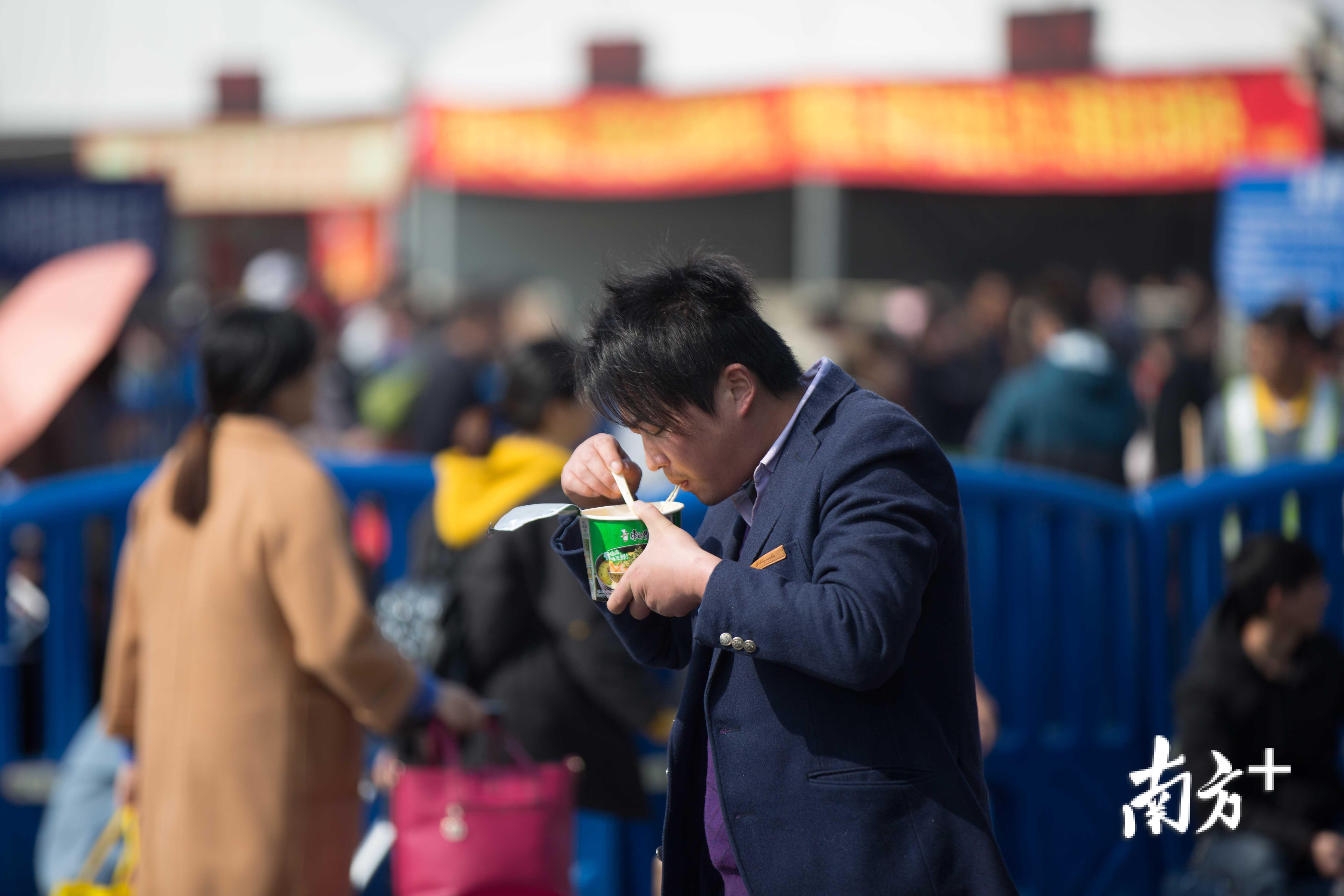 中午两点的火车站广场上，一位候车的旅客正站立着吃方便面。