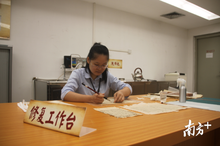 张月兰在修复工作台上用毛笔修复书页。