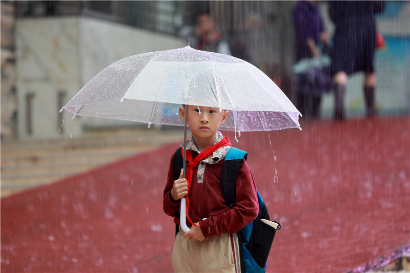 一名学生放学后打着雨伞在雨中发呆