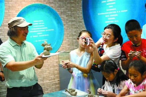 钟汝荣（左）与观展市民互动，展示石湾陶塑的制作手法。束维摄