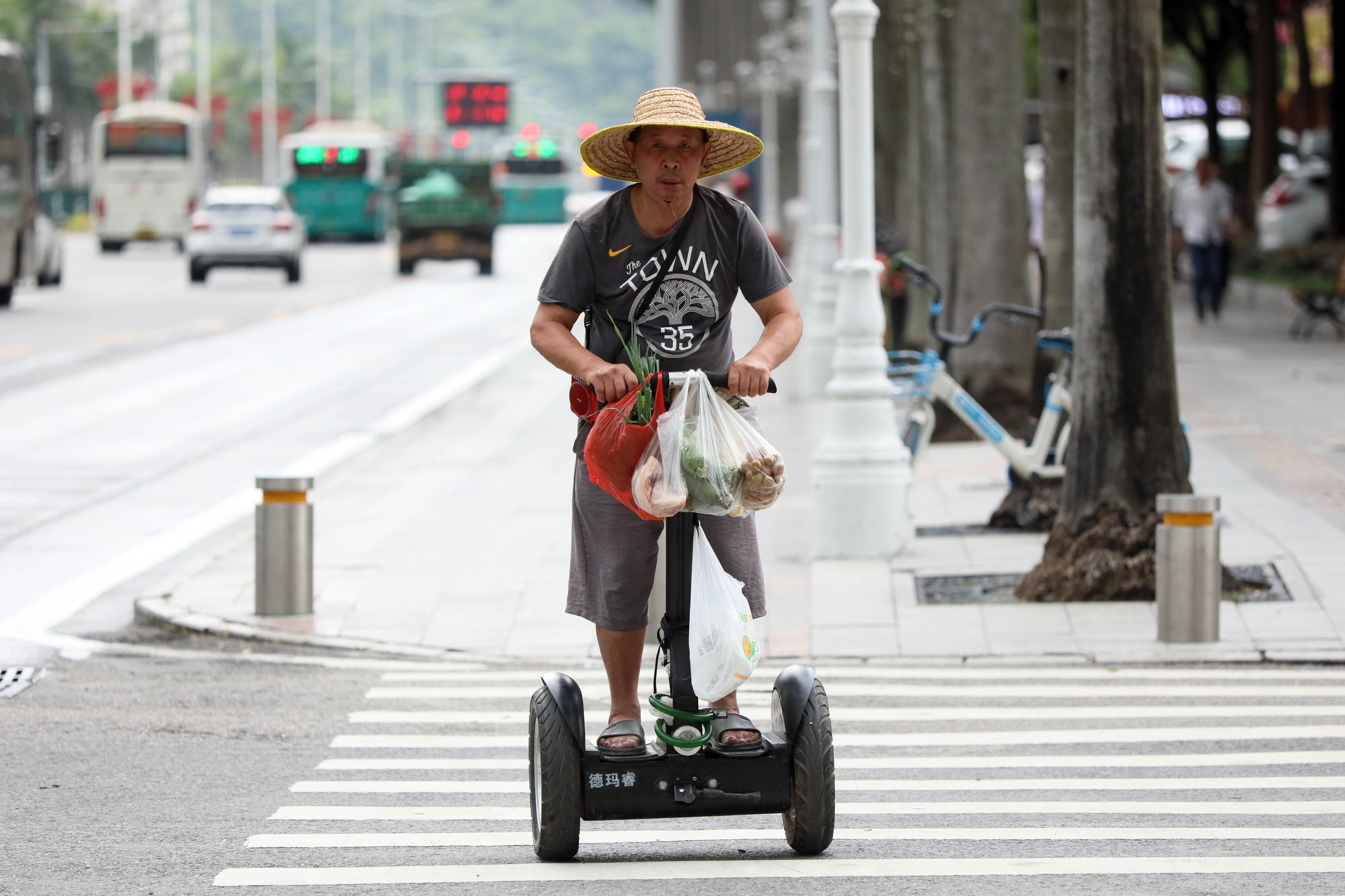 一位阿伯戴著草帽踩著滑輪車去買菜.