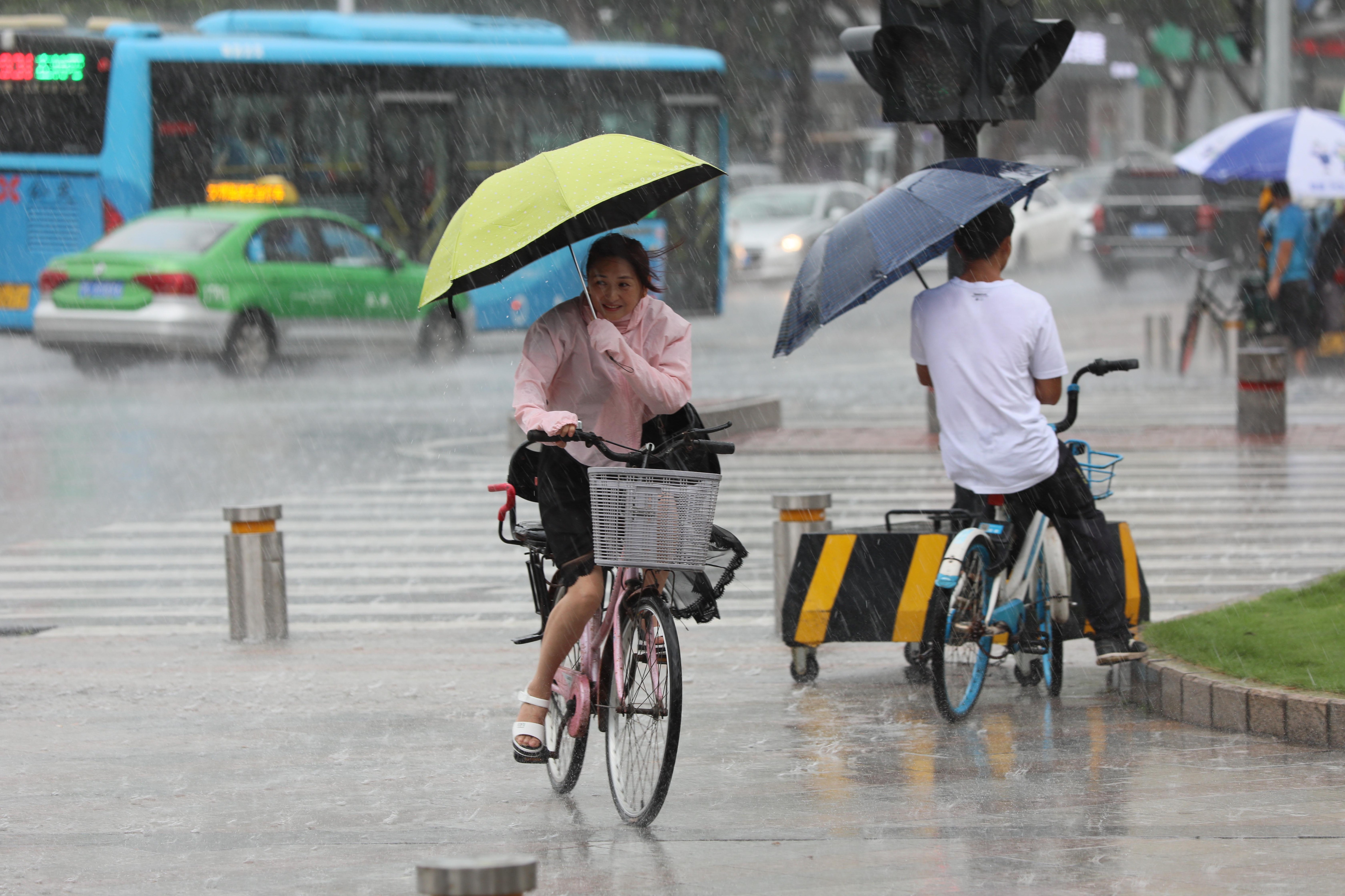 女子撑着伞,骑着单车雨中小心前行