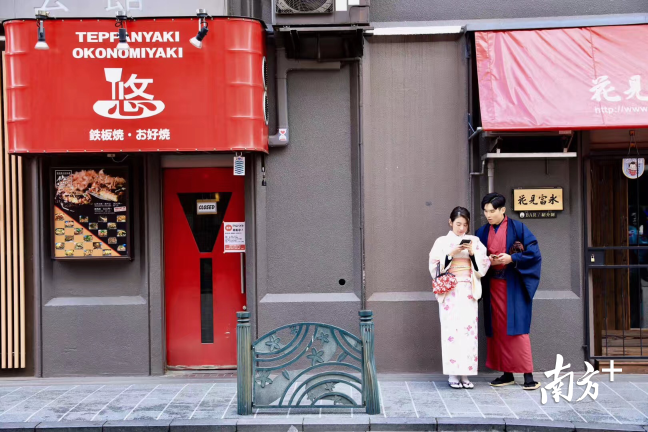 餐饮店前,一对行人穿着日本当地的特色服装。 餐饮店前,一对行人穿着日本当地的特色服装。