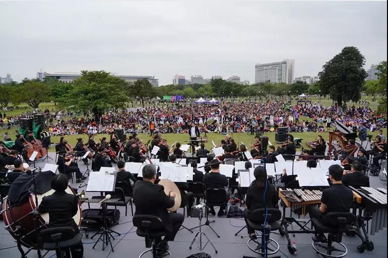图为参展作品。在清风绿草的怀抱中，在高楼与绿树间，伴随着交响乐团的悠扬琴声与艺术家们曼妙的歌声，东莞的市民们纷纷停驻、席地而坐，轻松享受音乐盛宴。龚名扬 摄