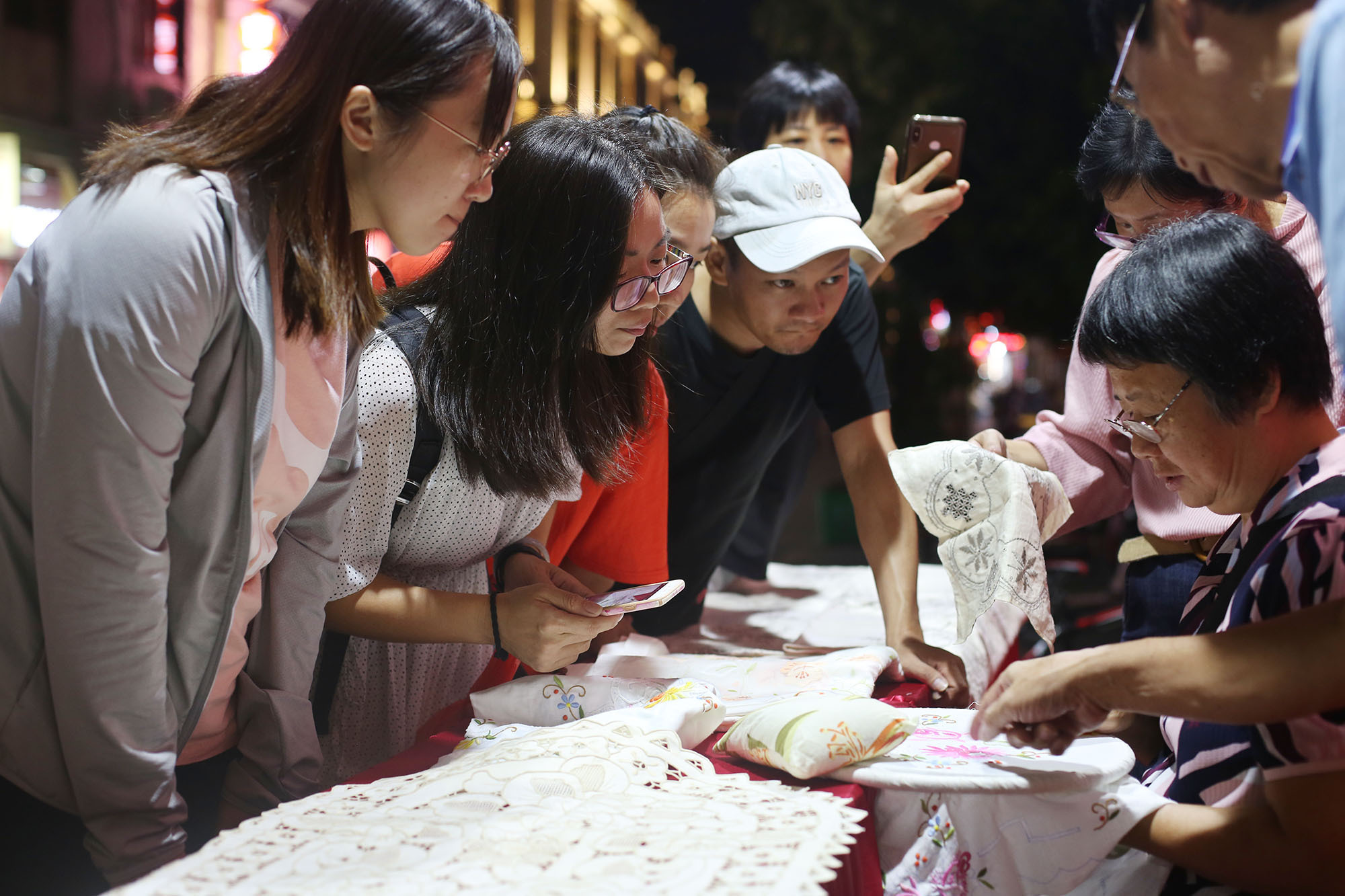 国家级非遗项目潮州抽纱代表性传承人薛建铭在潮州牌坊街演示抽纱技艺，引得年轻人俯身仔细观看。苏仕日 摄