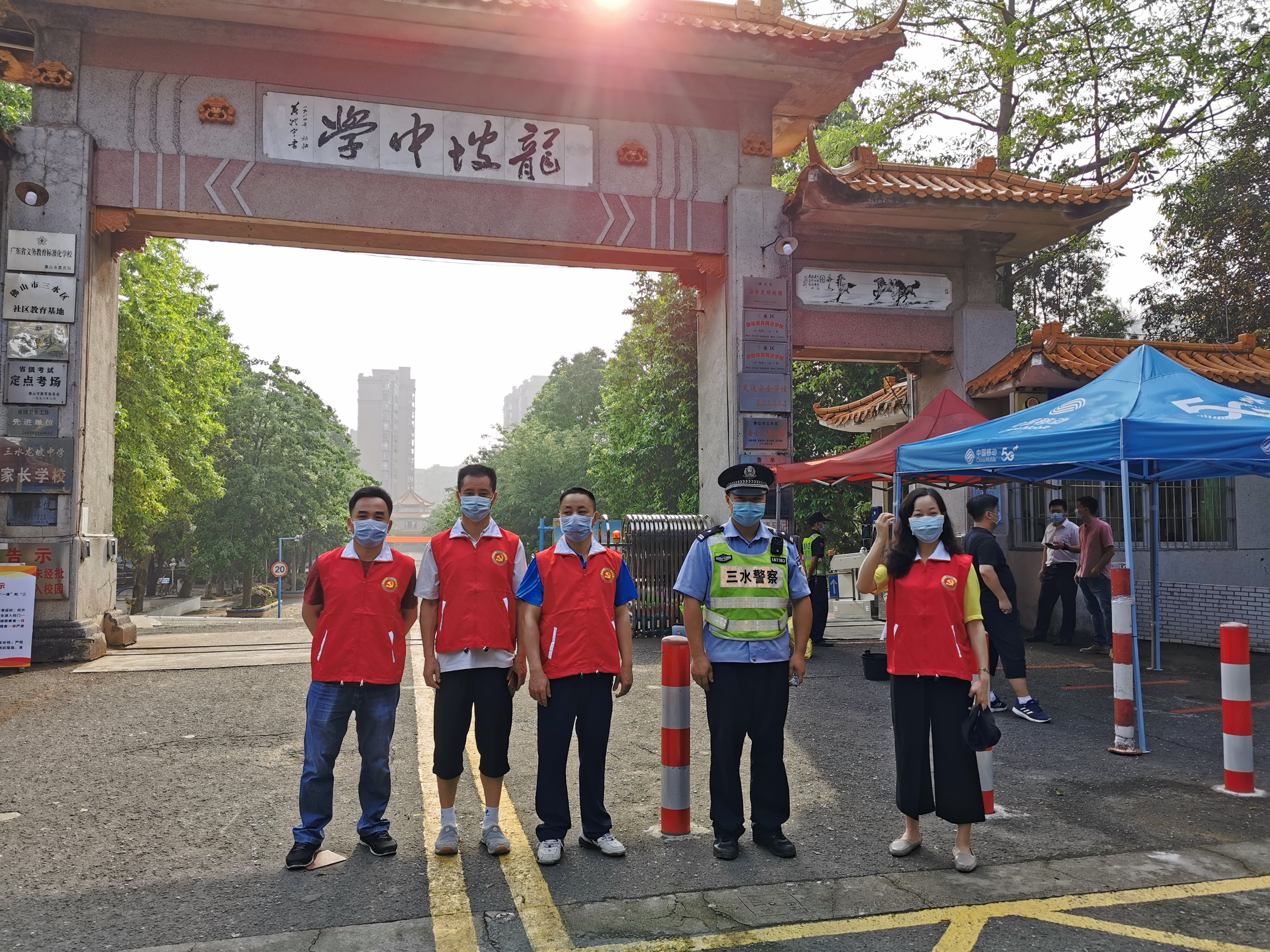 11日早上,在三水区芦苞镇龙坡中学校门口,身穿红马甲的党员志愿服务队指导学生测温、帮助学生搬运行李。