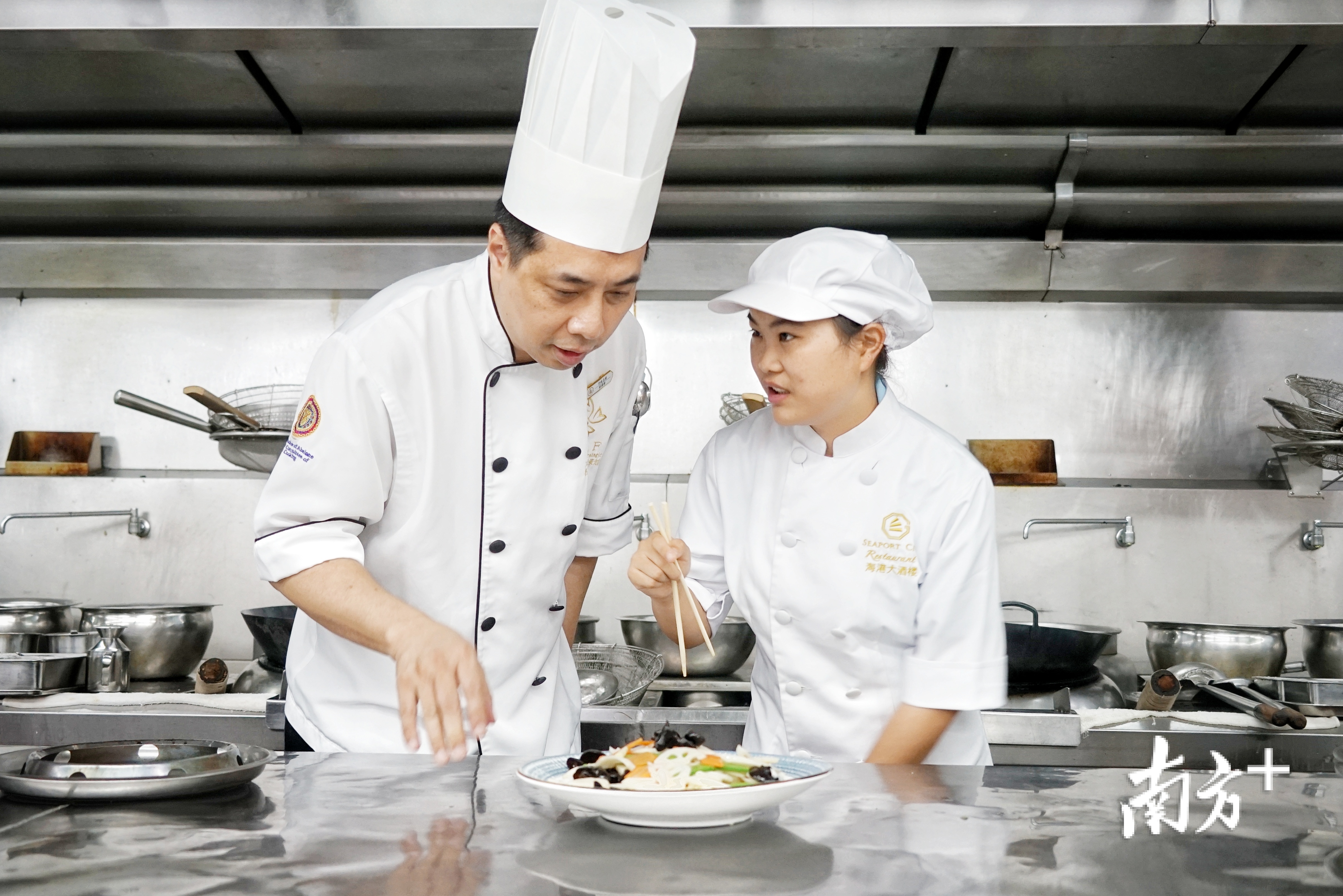 中山海港城海鲜大酒楼行政总厨欧建新(左)指导云南昭通籍学生徐友香制作粤菜。