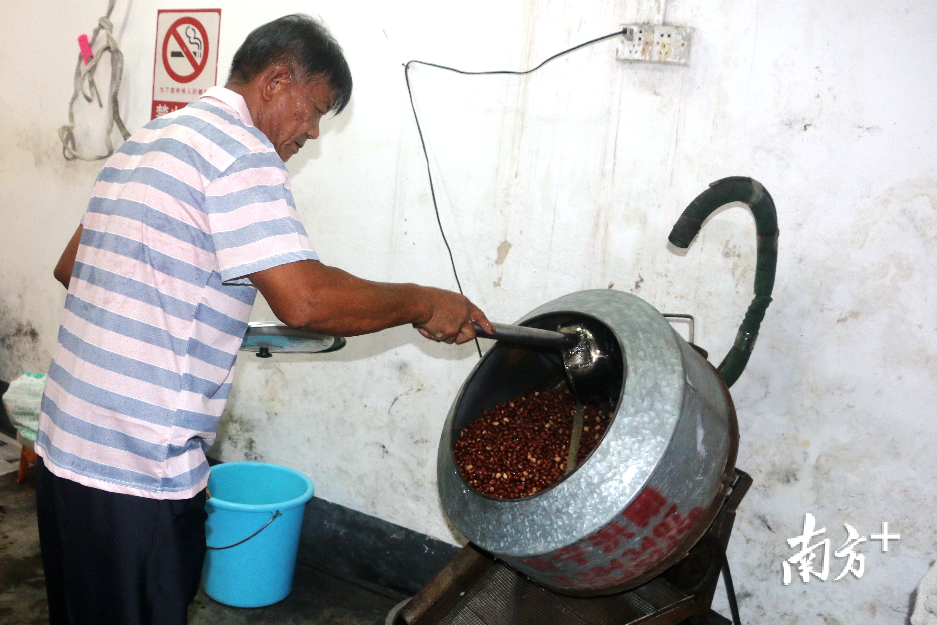 赵汉容将糖浆用瓢子分次加入滚筒中，让滚筒里炒熟的花生米“穿上”糖衣。