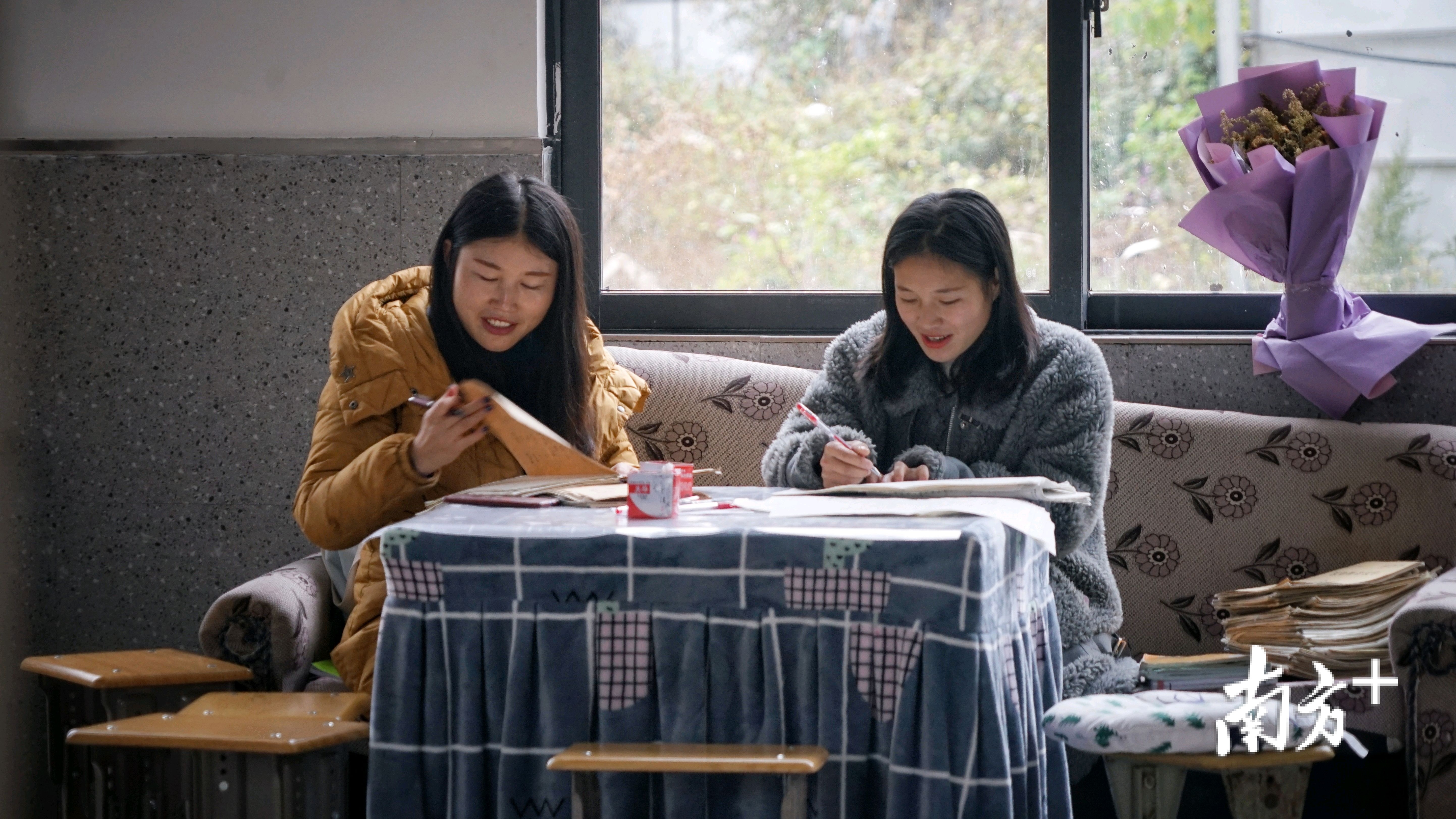 老师们在简陋的办公室里批改学生作业,脸上充满笑容。