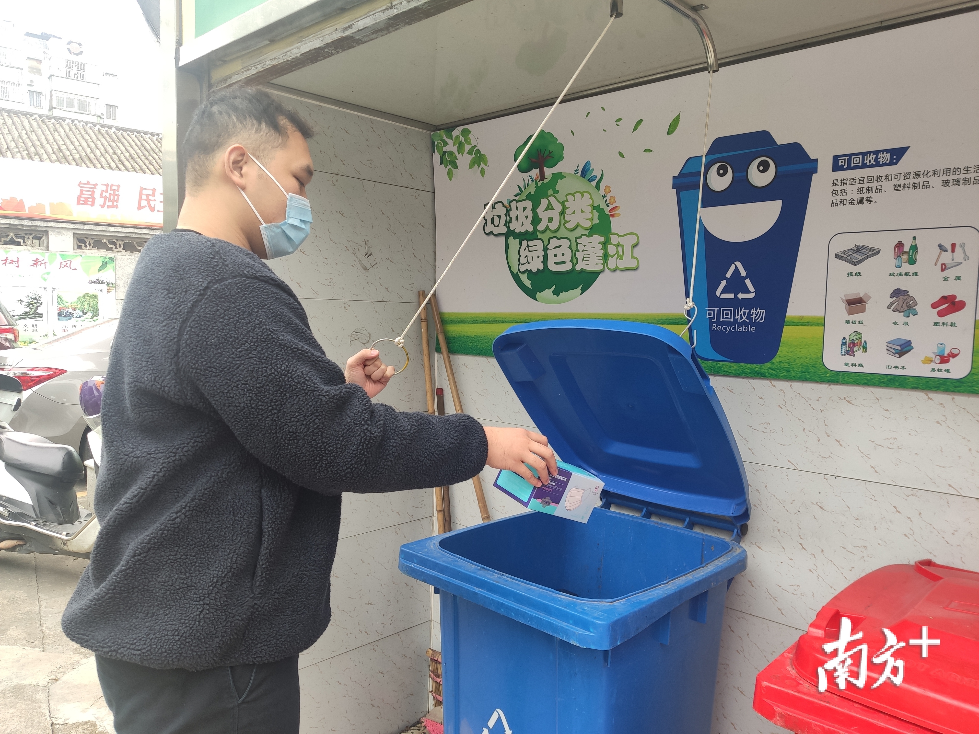 市民拉开垃圾桶盖子扔垃圾。