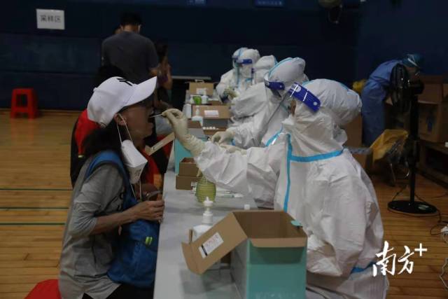 【海珠体育中心】提醒：分批次凭预约号采样检测，避免扎堆在海珠体育中心的核酸检测点，素社街道的居民在羽毛球馆内排队检测核酸，室内控制在100人左右，整体有序。为了提高效率，等候通道上摆放了一些凳子，提供给有需要的居民。同时，每隔几米就张