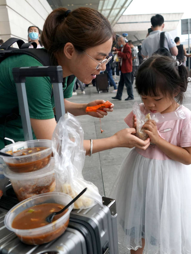 7月21日，一名滞留旅客在郑州东站进站口处喂孩子吃早餐。