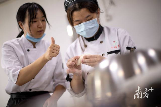 中点课程上，点心老师竖起大拇指手势鼓励正在学习包饺子的聋生。