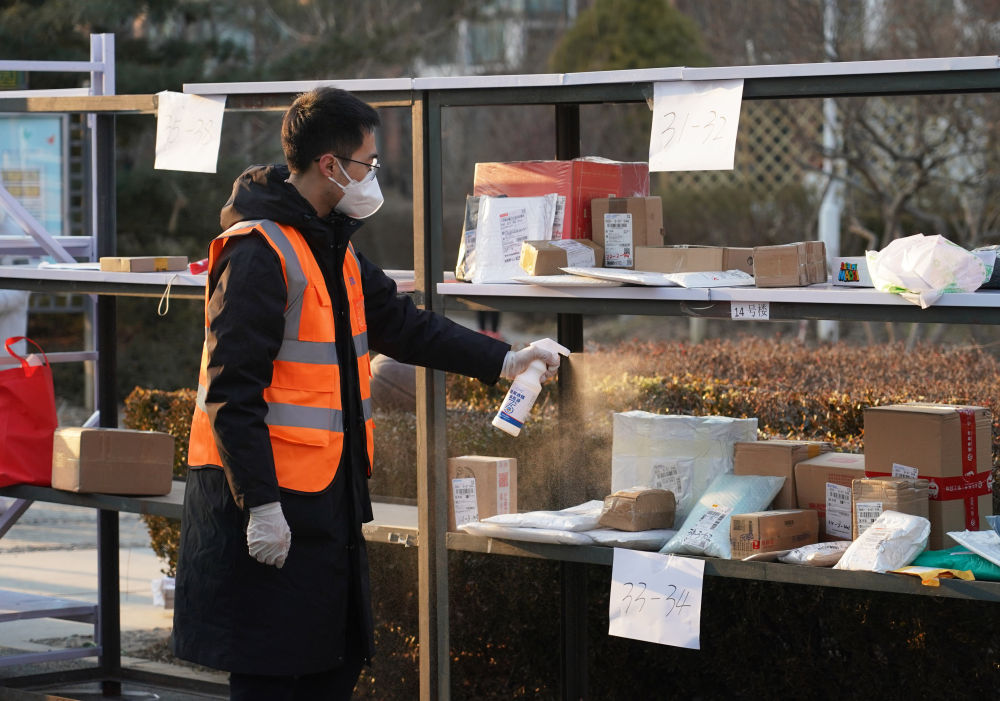 1月18日，北京市海淀区马连洼街道永丰路百旺茉莉园一期外，工作人员对快递进行消毒。（新华社记者任超 摄）