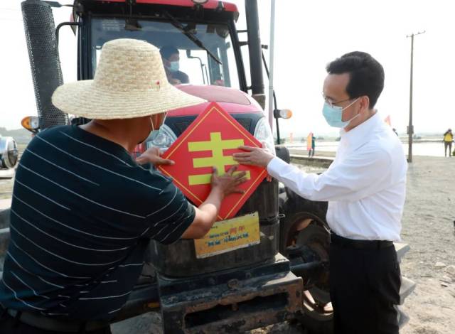 2022年3月15日，在高要区南岸街道新江二村春耕现场，张爱军和绿行蔬菜种植基地负责人一起在一辆拖拉机车头上贴上“丰”字，送上美好祝愿。