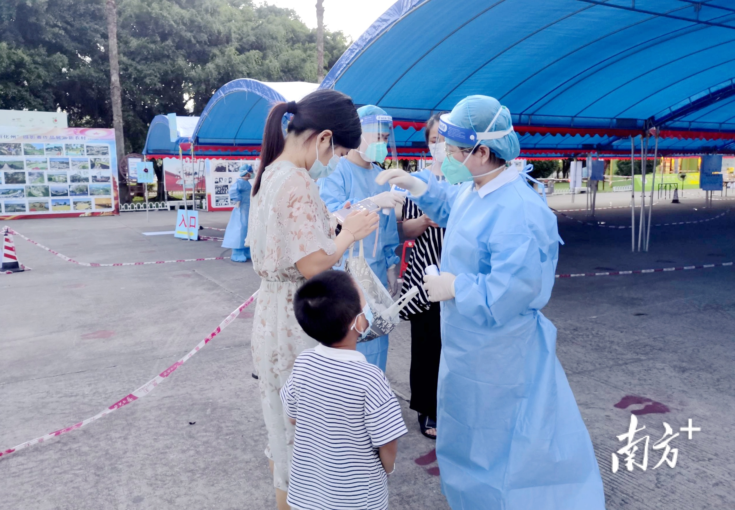 化州市税务局疫情防控党员突击队志愿者在化州市康景体育馆“黄码”专区检测点引导前来核酸检测的群众进行测量体温、有序排队、扫码、登记。