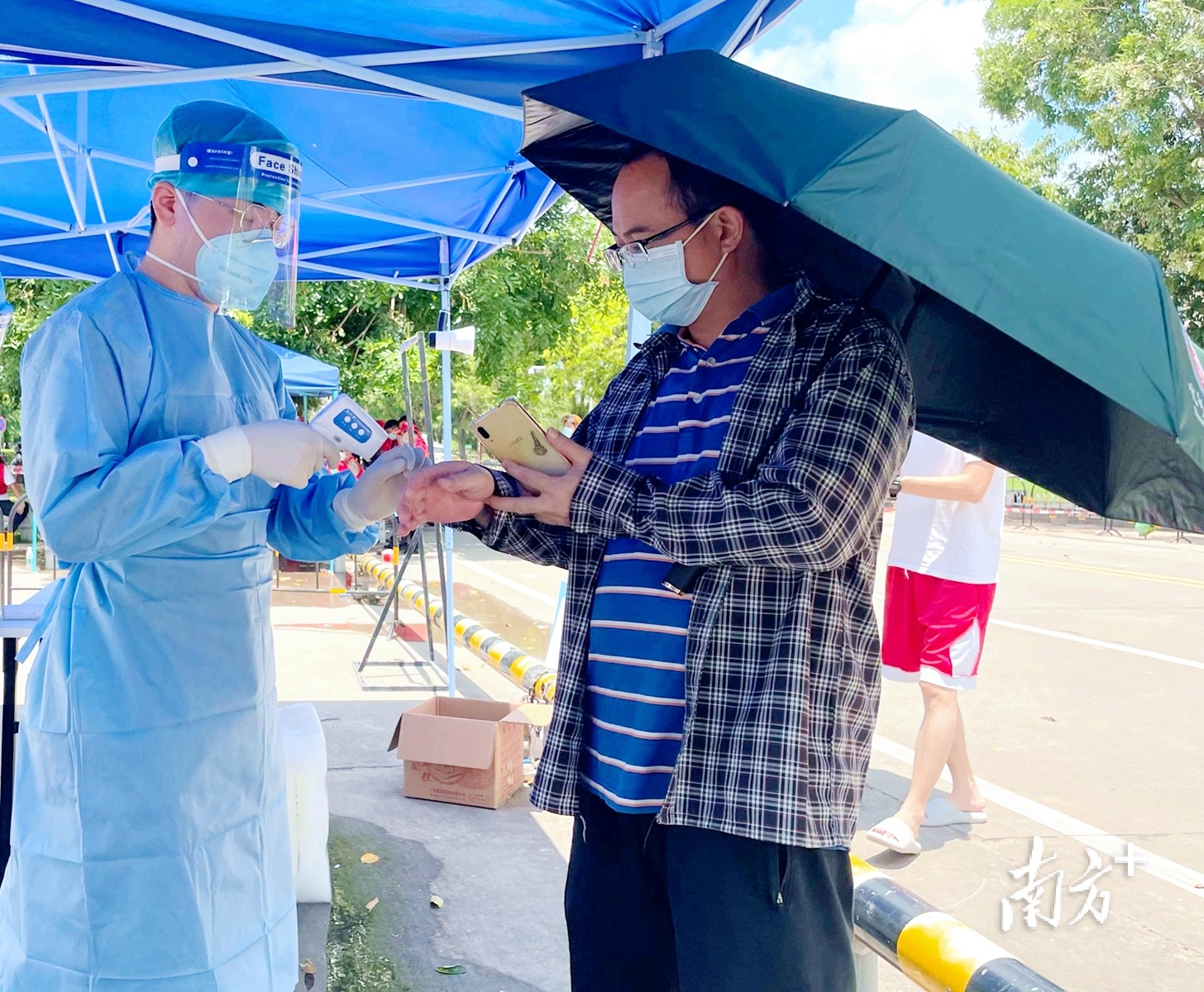 化州市税务局疫情防控党员突击队志愿者在化州市康景体育馆“黄码”专区检测点为前来核酸检测的群众测量体温。