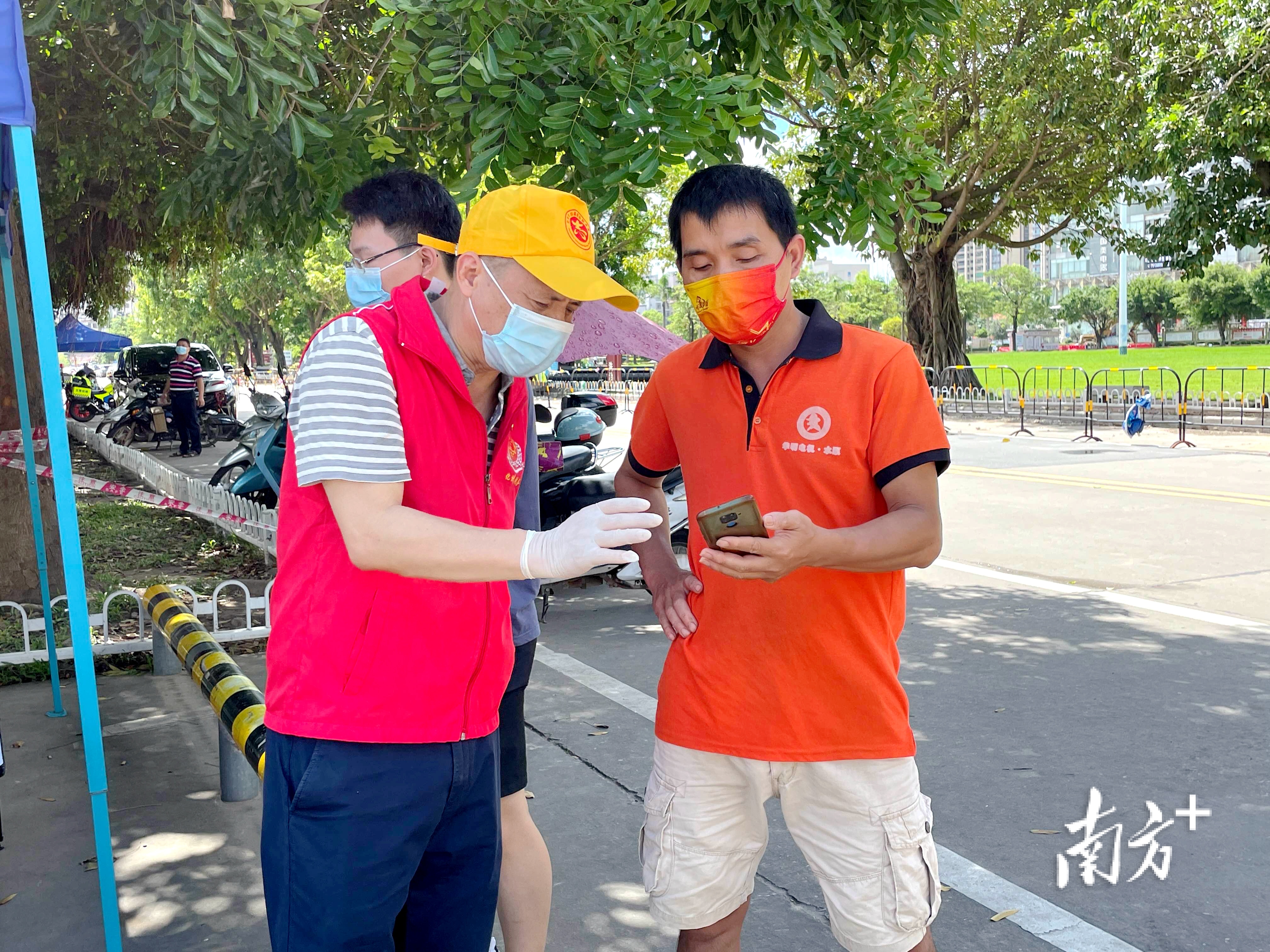 化州市税务局疫情防控党员突击队志愿者在化州市康景体育馆“黄码”专区检测点引导前来核酸检测的群众登记信息。