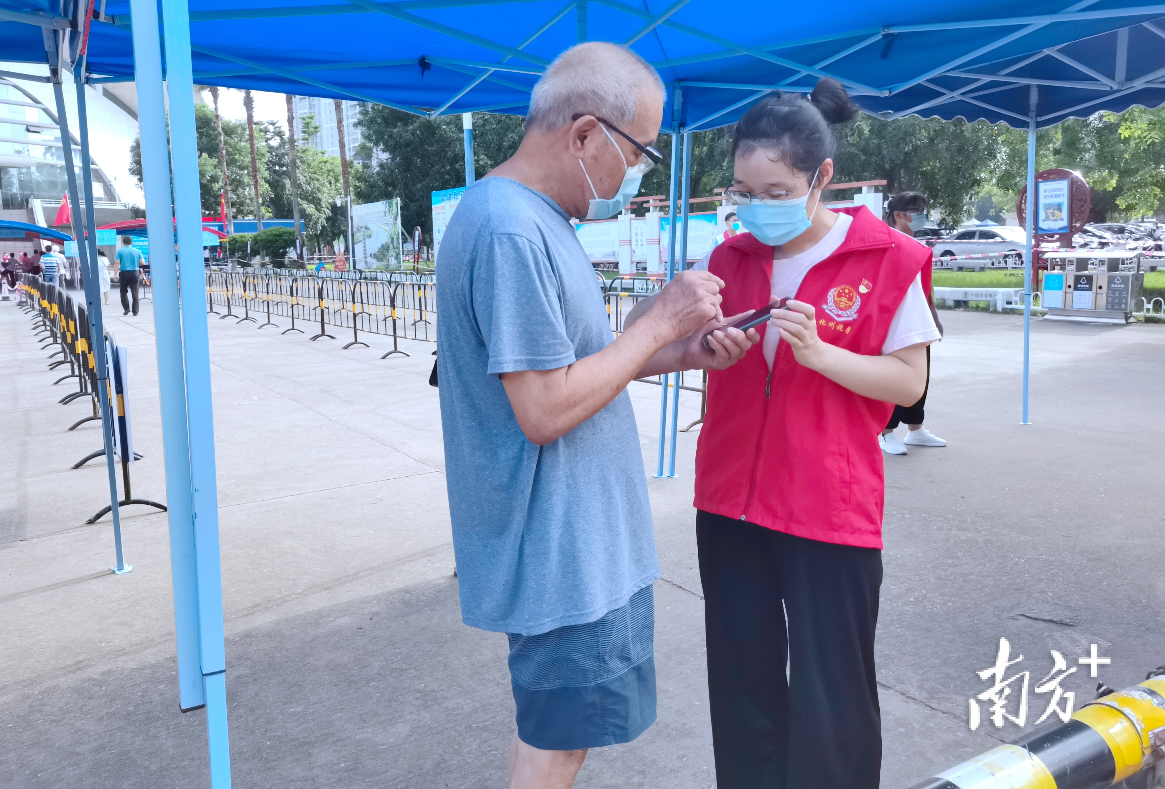 化州市税务局疫情防控党员突击队志愿者在化州市康景体育馆“黄码”专区检测点引导前来核酸检测的群众提前打开“粤核酸”小程序登记信息。