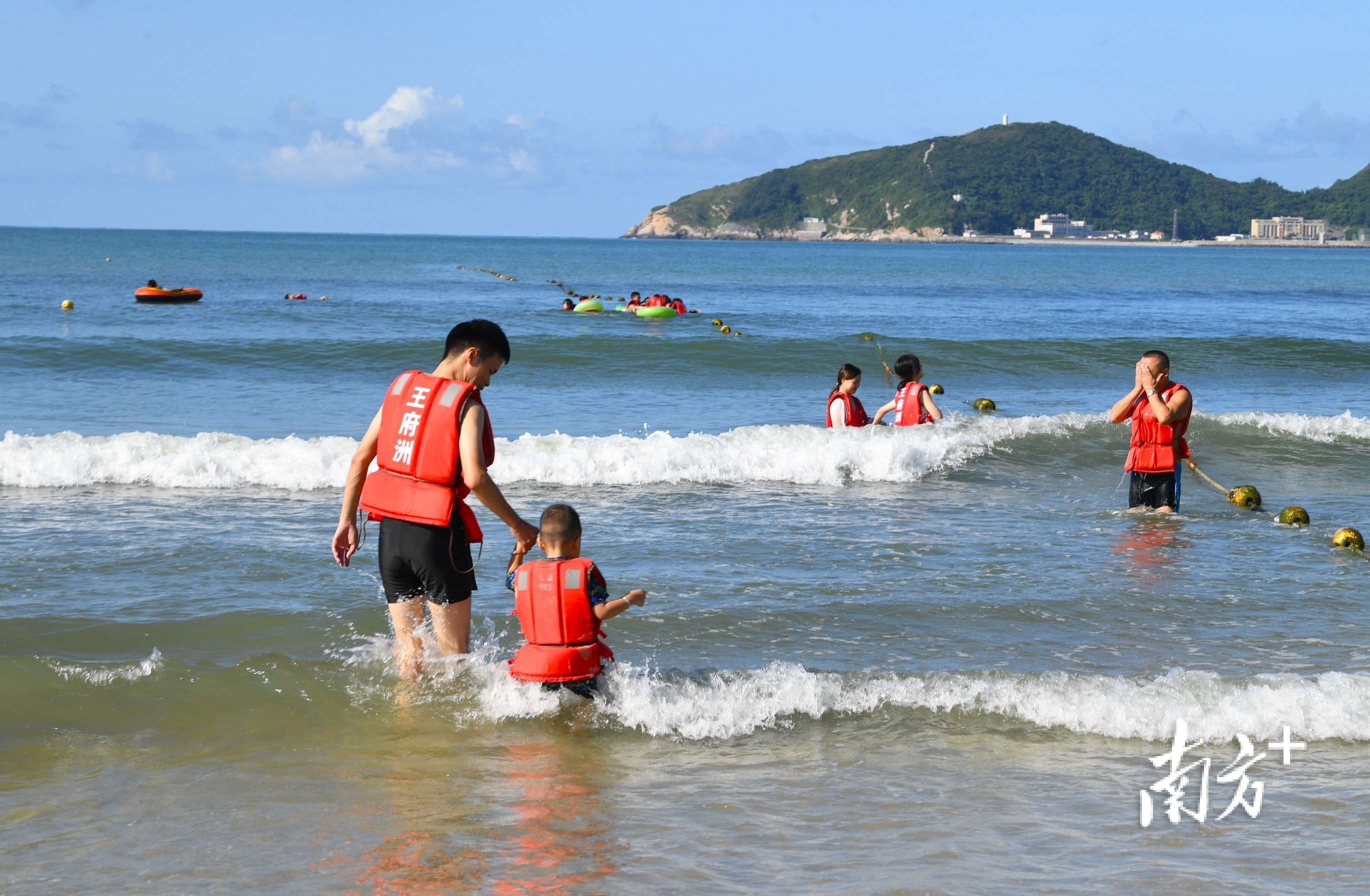 一名父亲带着小孩勇敢走向海水深处。 南方+ 杨兴乐 拍摄