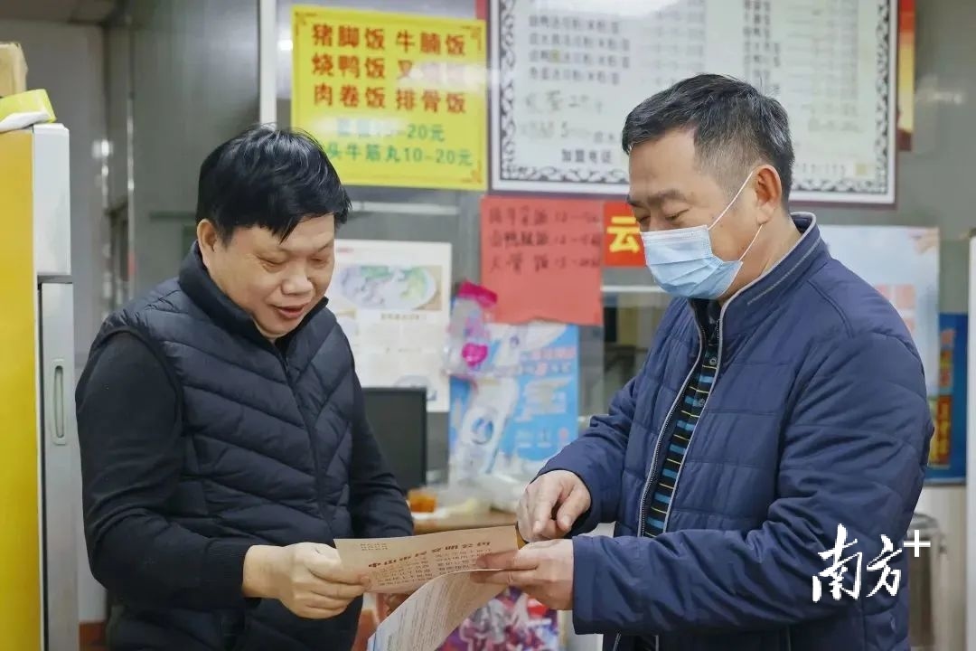 何大庆（右）向店铺负责人宣传落实“门前三包”工作。