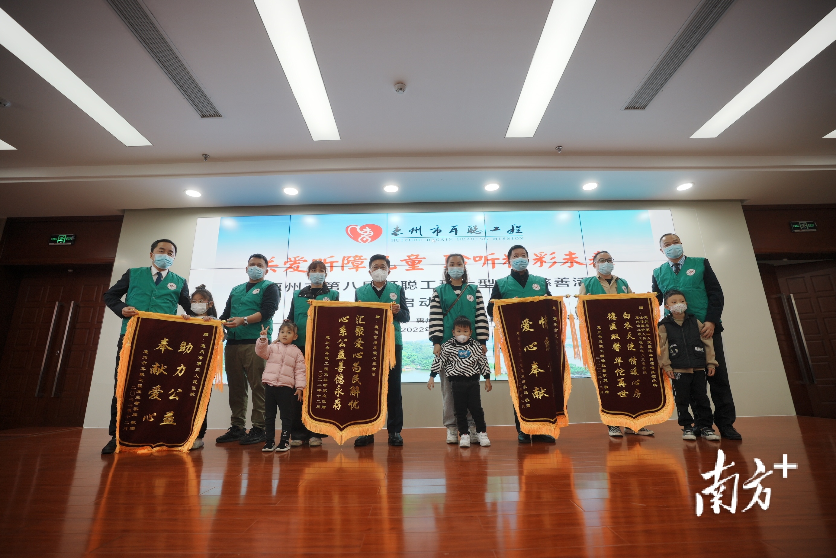 听障儿童和家长代表向惠州市慈善总会、惠州市第三人民医院等赠送锦旗,图中第二排右一为惠州市耳聪工程创始人王豪