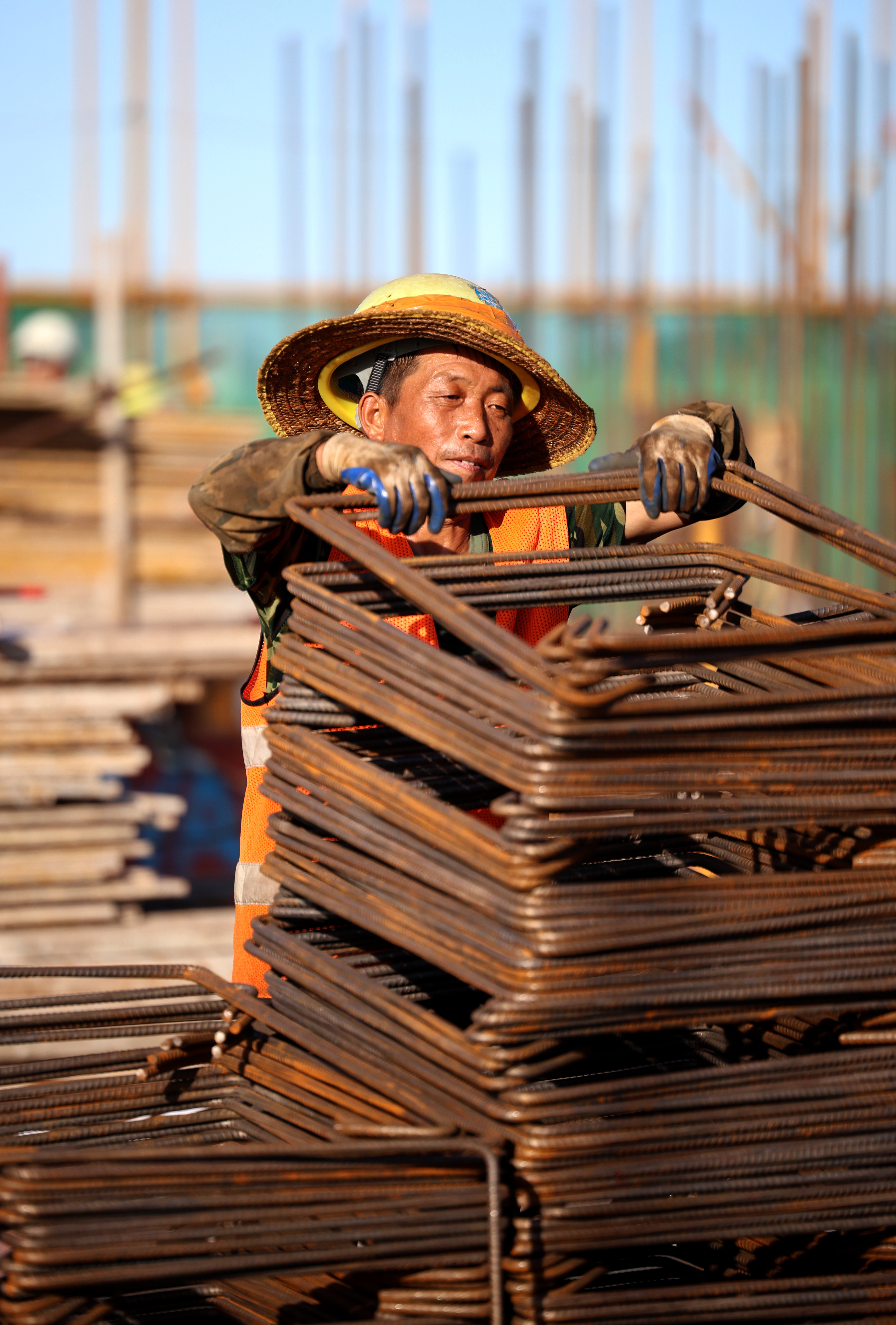 工人正忙着搬运钢筋，他的脸被晒成与钢筋同一个色系。