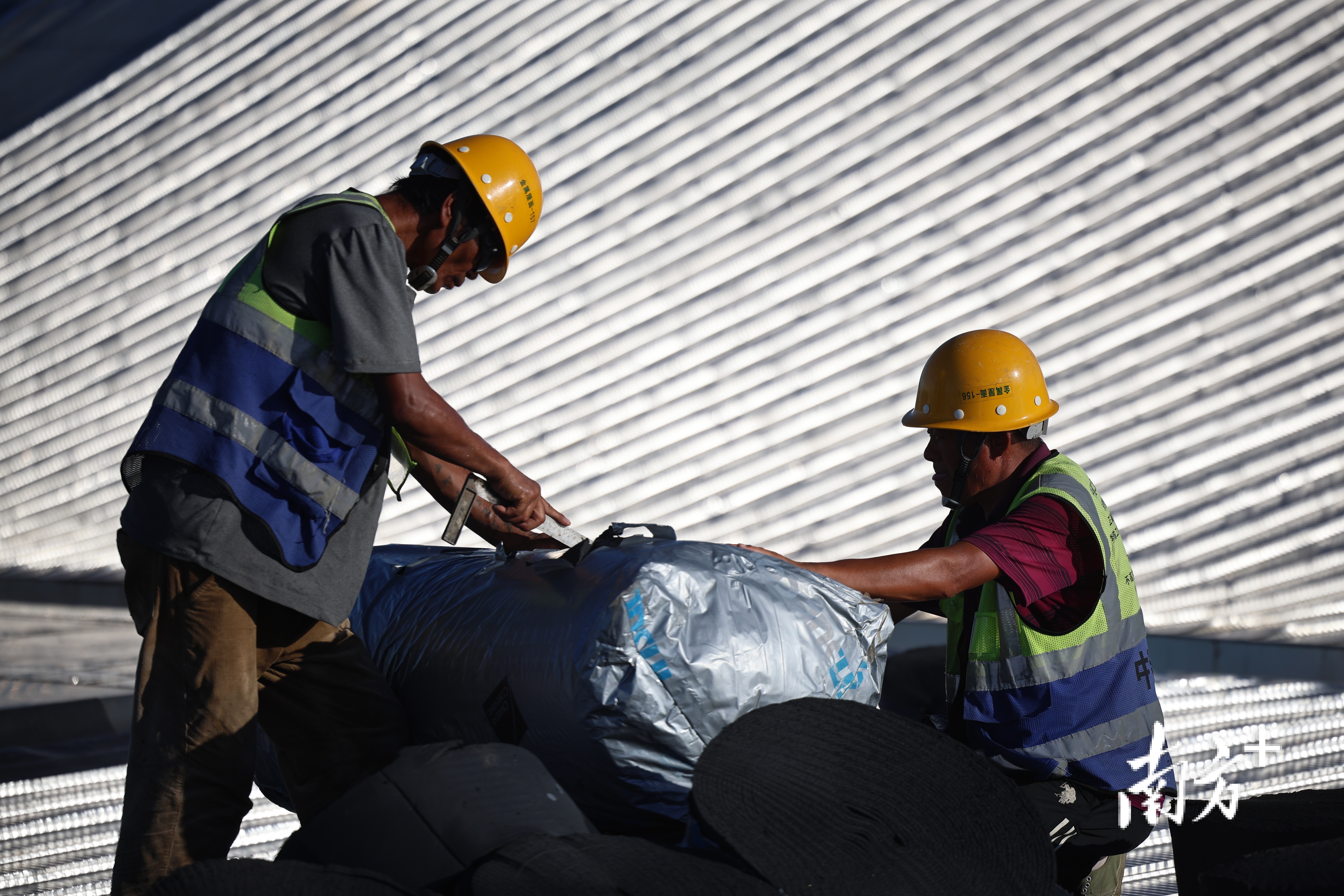 工人在切割屋面铺设的材料,他们的身后是热辣的阳光反射。 工人在切割屋面铺设的材料,他们的身后是热辣的阳光反射。