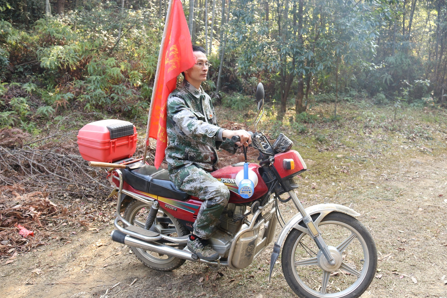 刘天娇骑着摩托车上山，河源护林护喇叭循环播放着警示语