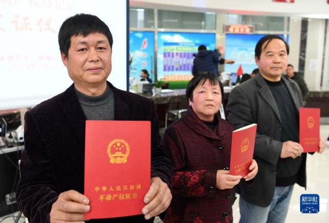 在安徽省宣城市旌德县首本农村宅基地“三权分置”不动产权登记证发证仪式上，宅基地使用权人王五四(左)，宅基地资格权人方圣莲(中)和宅基地所有权人、旌德县兴隆镇大礼村民委员会代表孙秀宝展示领到的农村宅基地“三权分置”不动产权证书(2018年2月27日摄)。新华社记者 刘军喜 摄