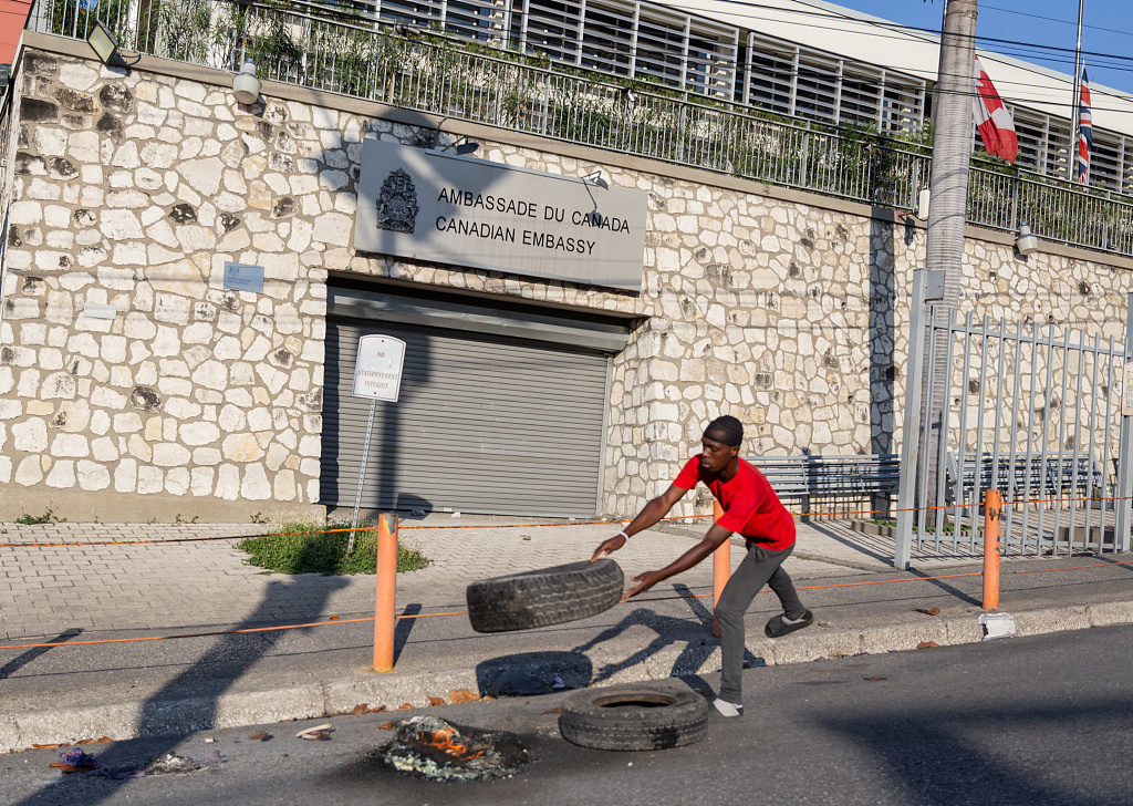 当地时间2024年3月7日,海地太子港,一名男子在要求海地总理阿里埃尔·亨利辞职的示威活动中,将一个轮胎扔进了加拿大大使馆前的火中。 当地时间2024年3月7日,海地太子港,一名男子在要求海地总理阿里埃尔·亨利辞职的示威活动中,将一个轮胎扔进了加拿大大使馆前的火中。